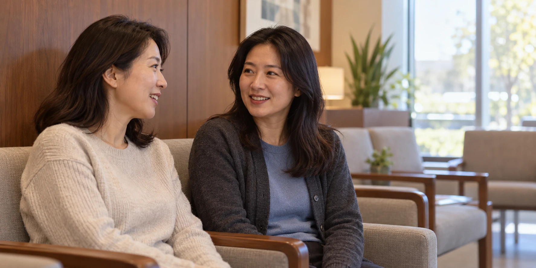 치과 대기 공간의 나무 팔걸이 의자에 나란히 앉아 편안히 대화하는 성인 여성 두 명