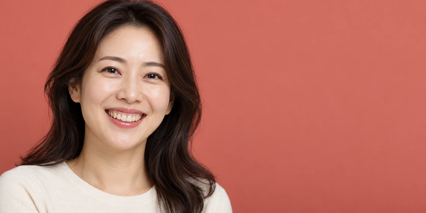 코랄색 배경 앞에서 크림색 셔츠를 입고 자연스럽게 미소 짓는 여성의 상반신