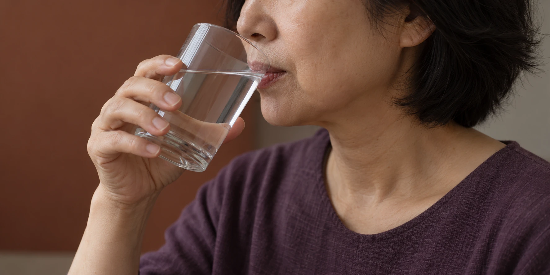 Side view of a middle-aged woman drinking from a glass of water in a calm indoor setting